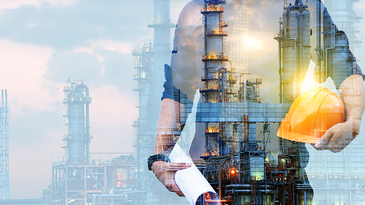 An engineer holding a hard hat and blueprints with an image of an oil refinery in the background.