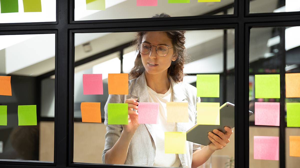 An image of a woman project managing with multiple sticky notes on a window 