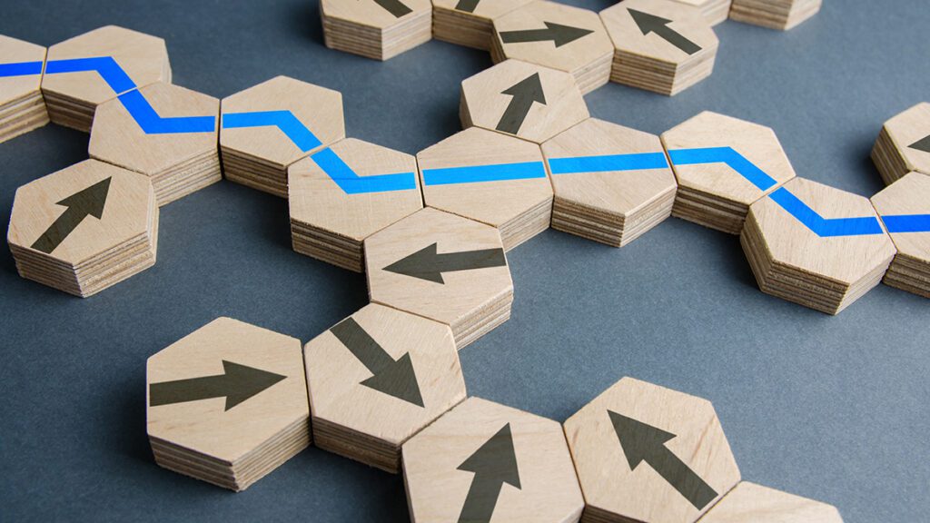 Hexagon wood tiles placed together forming a path for customer success. The blocks have arrows on them and several have a blue line on them that connect to form a path.