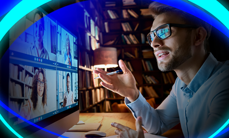 man looking at desktop monitor filled with team member, having a discussion. Has pen in hand, mouse is on desk.