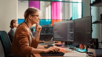 female at desktop with two monitors looking at code
