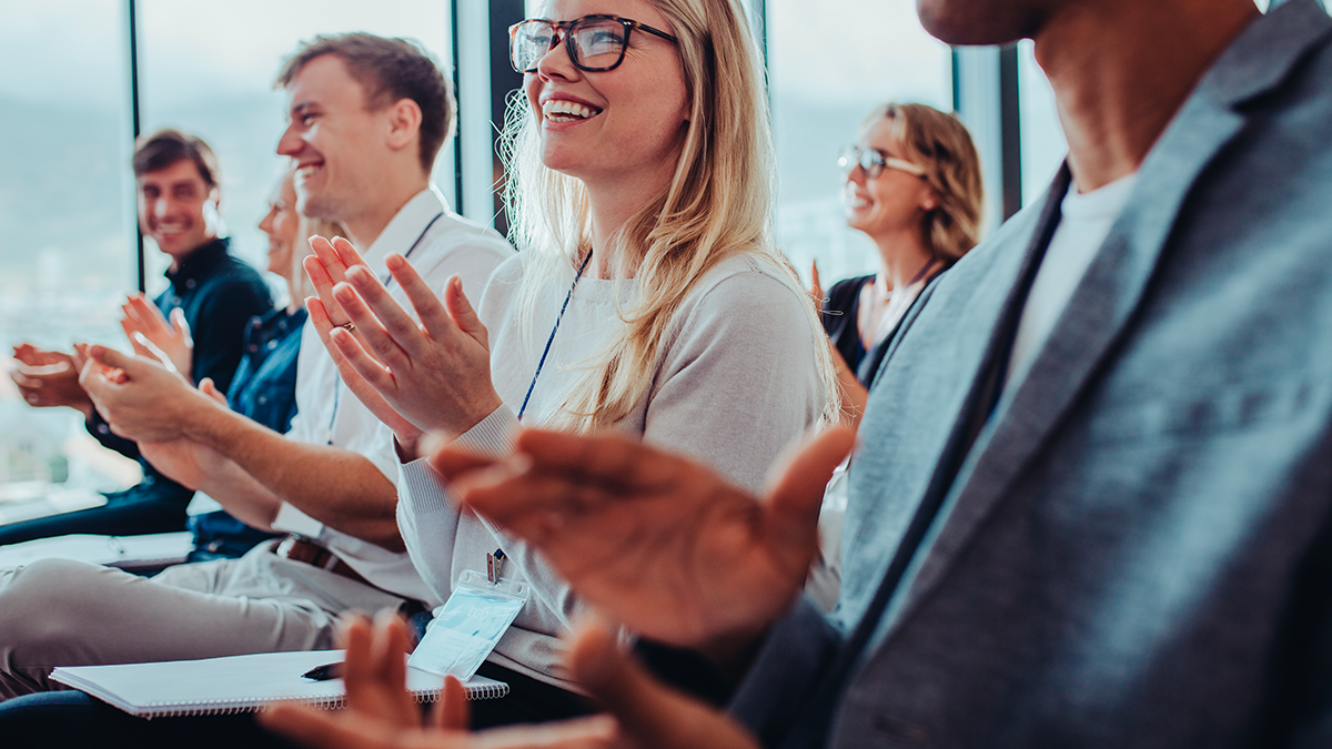 A group of professionals clapping as they site and watch a live presentation like the Content Cloud tracks at OpenText World 2023
