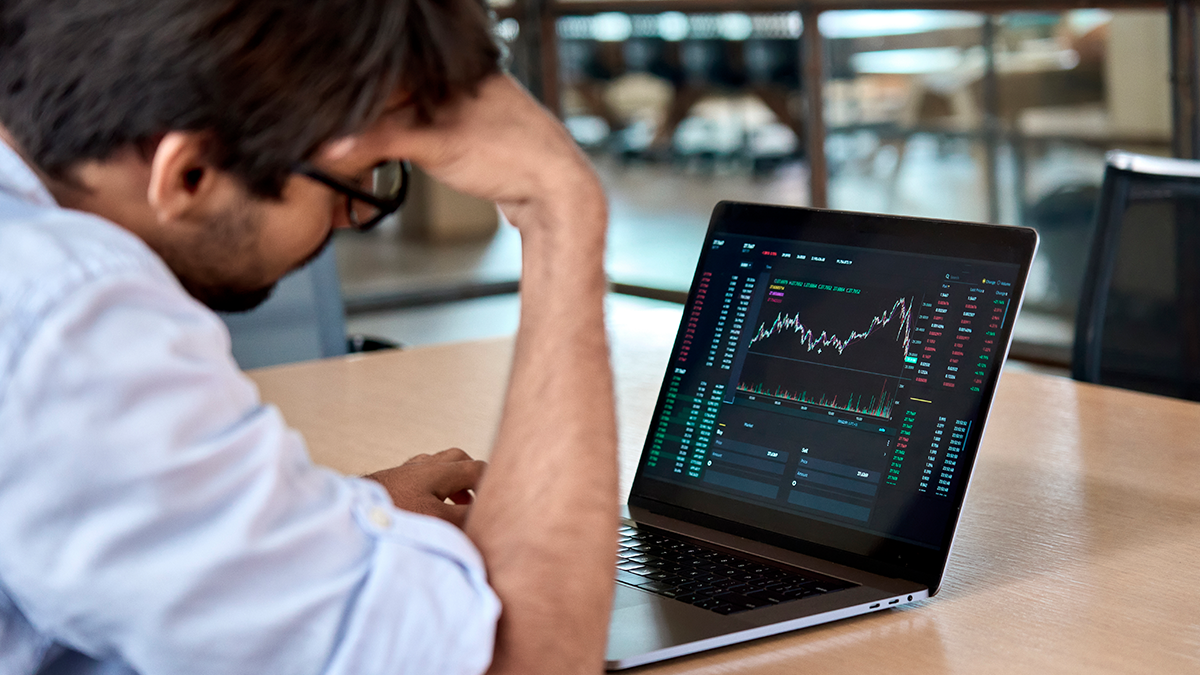 Male professional looking at graphs on a laptop to analyze economic recession.