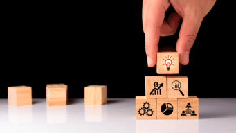 Close-up of a person's fingers holding onto a small wooden block to complete a pyramid of blocks to show how intelligent insights build foundations