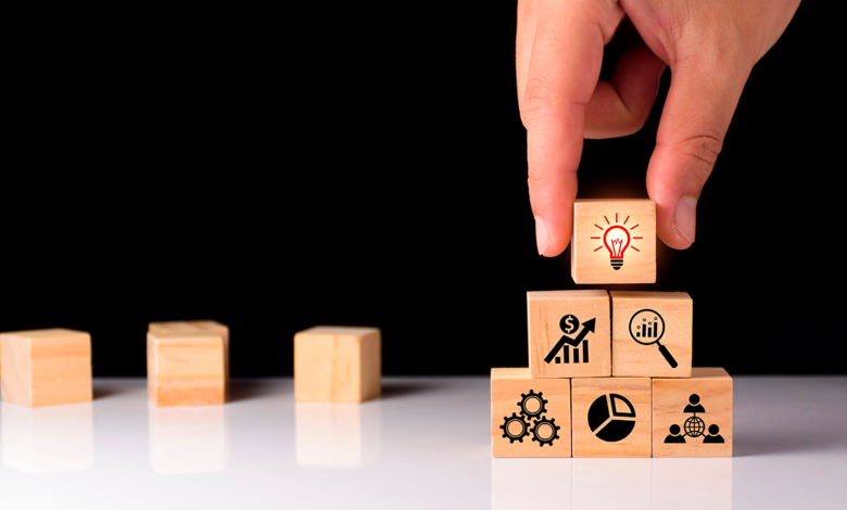 Close-up of a person's fingers holding onto a small wooden block to complete a pyramid of blocks to show how intelligent insights build foundations