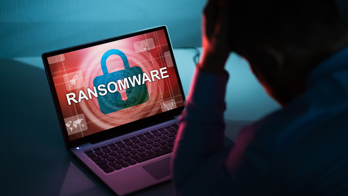 man looking at laptop with head in hands, laptop screen is red with a giant lock and the word ransomware written across it
