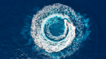 aerial shot of a boat driving in circles creating a big circle of white waves