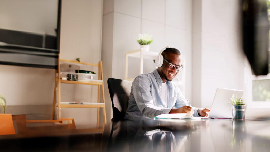 remote african-american marketer thrives enjoying virtual training; he is sitting at a table in his condo smiling, and he has sunlight coming into the room