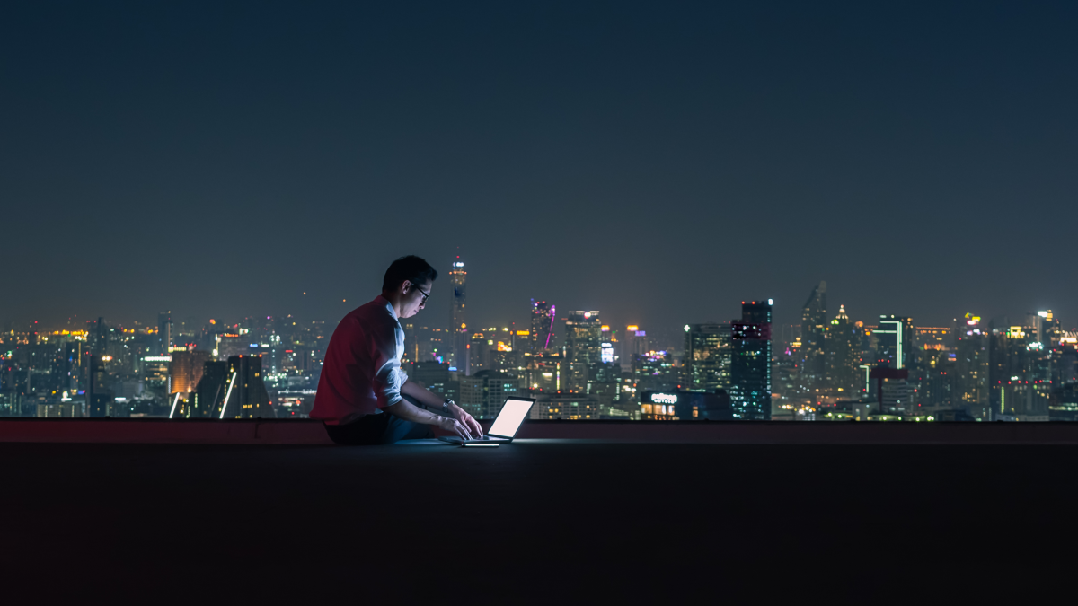 Man on a laptop in front of a night cityscape