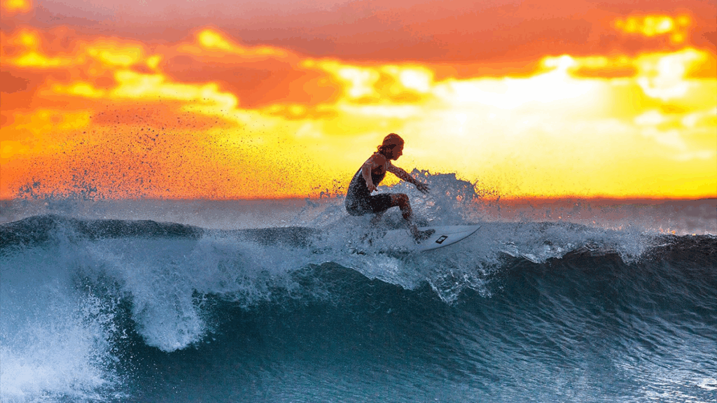 Sunset with orange and yellow sky. Female surfer riding a wave on the ocean