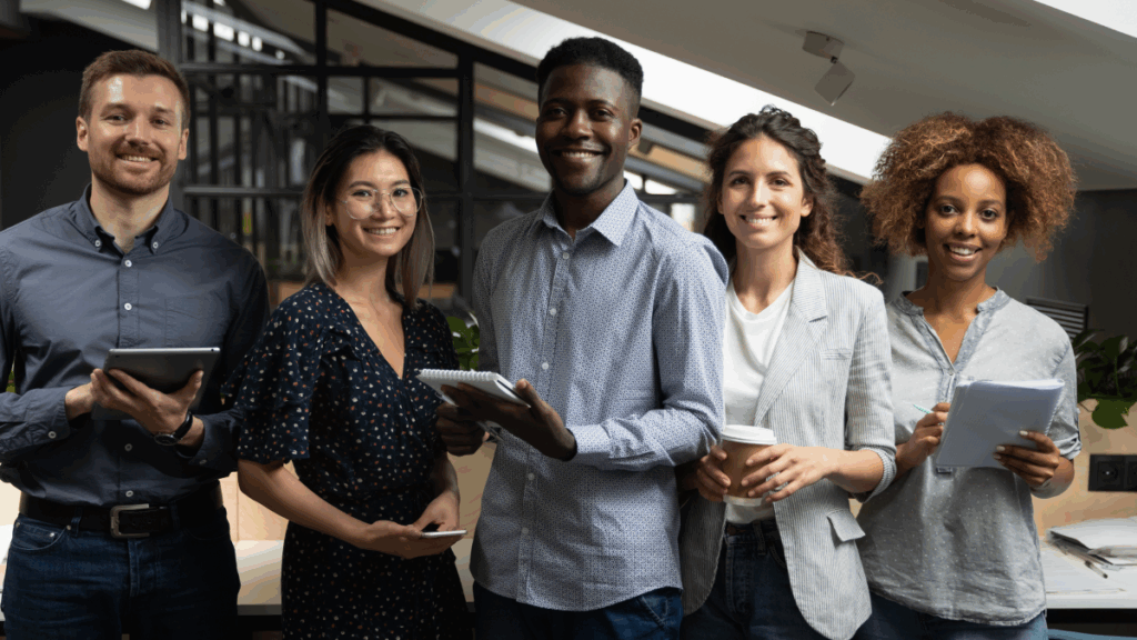 group of 5 diverse developers, each holding a device, smiling into the camera to celebrate National Developers Day, a day that focuses on developer experience (DevEx)
