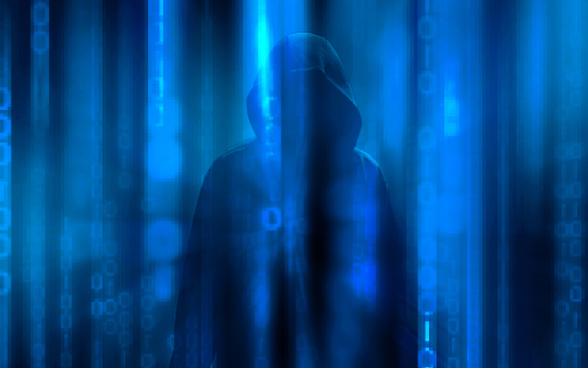 An image of a hacker behind a curtain representing the hidden risk of ransomware.