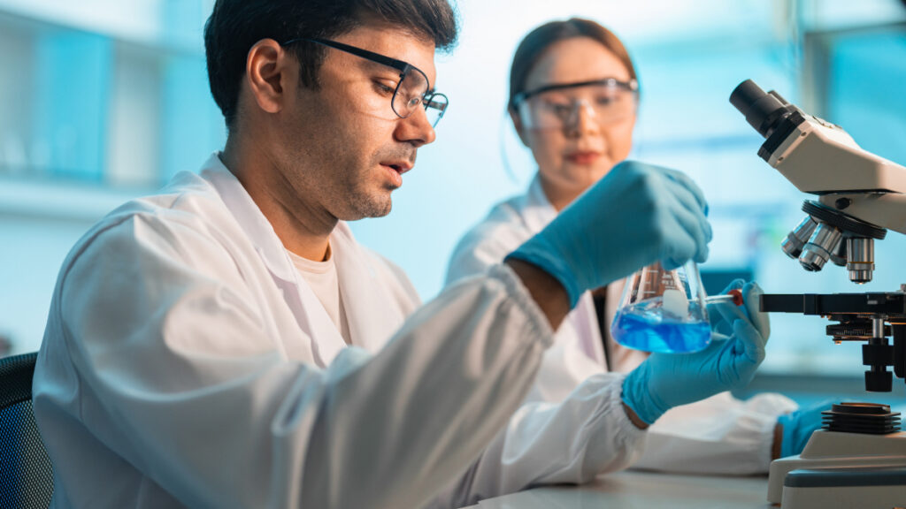 Lab techs working with a beaker and microscope
