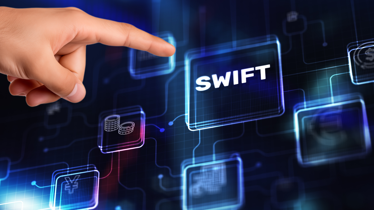 dark background with transparent screen showing "SWIFT" icon and man's finger about to press it; indicates a financial messaging hub.