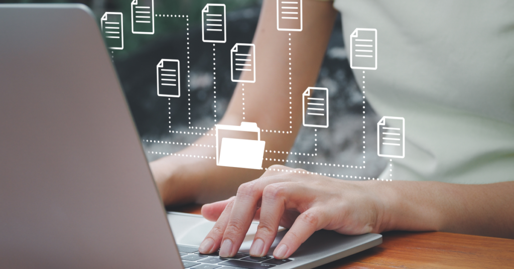 A female worker's hands at a laptop keyboard with file and connectivity icons floating above it indicating the latest B2B integration Essentials updates: automated EDI workflows, expanded trading partner support, and multilingual tools built for growing SMBs.