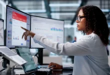 female employee working at two monitors, looking at treasury infrastructure and operations dashboards