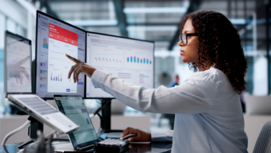 female employee working at two monitors, looking at treasury infrastructure and operations dashboards